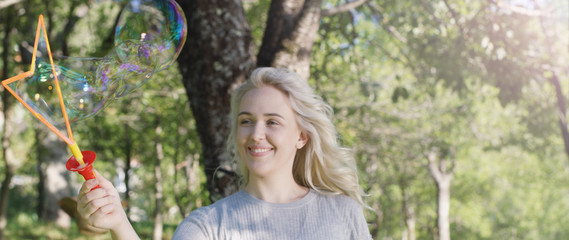 Gorgeous young brunette girl blowin soap bubbles in sunlit park.