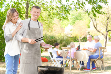 Man with wife cooking tasty steaks on barbecue grill outdoors