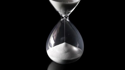 Falling sand showing the passing time of hourglass close-up and isolated on glossy black floor and background. Presented in the centre of the screen. - Powered by Adobe