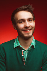 Male beauty concept. Portrait of smiling elegant young handsome man in green sweater posing over red background. Perfect skin. Stylish haircut. Hipster style. Close up. Studio shot