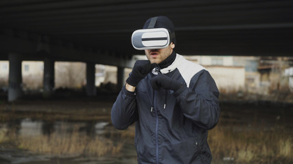 Martial boxing man in VR 360 headset training punches in virtual reality fight at urban location outdoors in winter