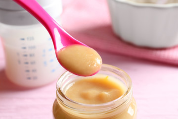 Jar and spoon with healthy baby food on table