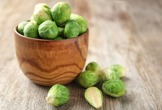 Bowl with raw Brussels sprouts on wooden background