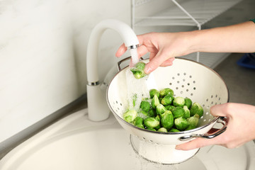 Woman washing raw Brussels sprouts in kitchen sink