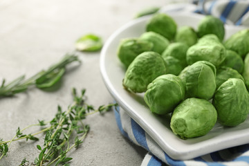 Plate with fresh raw Brussels sprouts and herbs on grey table, closeup