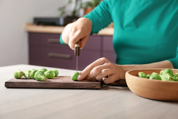 Young woman cutting fresh raw Brussels sprouts on board in kitchen