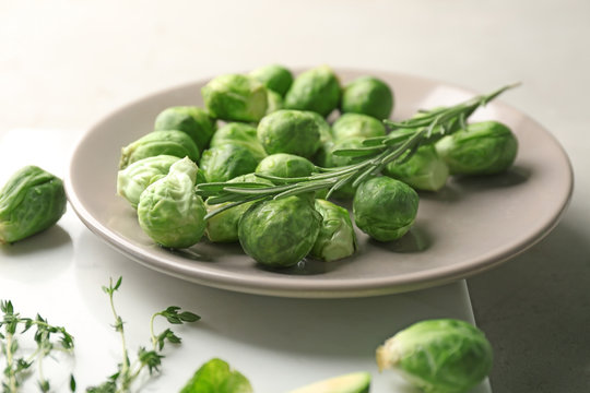 Plate with fresh raw Brussels sprouts and herbs on grey table, closeup