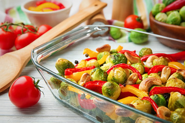Glass dish with baked Brussels sprouts, pepper and nuts on table