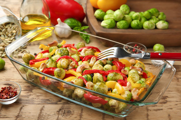 Fototapeta na wymiar Glass dish with baked Brussels sprouts, pepper and nuts on table