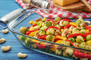 Glass dish with baked Brussels sprouts, pepper and nuts on table
