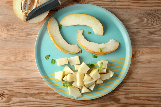 Plate with sliced yummy melon on wooden table