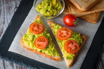 Avocado toast, cherry tomato on wooden background. Breakfast with toast avocado, vegetarian food, healthy diet concept.