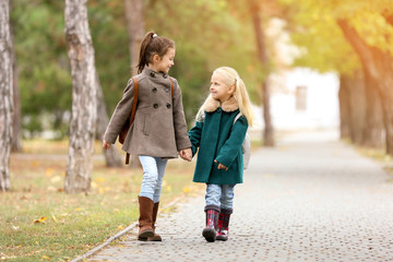 Cute little girls in outwear walking together in park