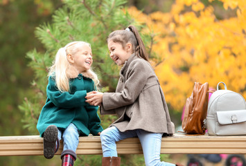 Cute little girls in outwear sitting and playing on bench outdoors