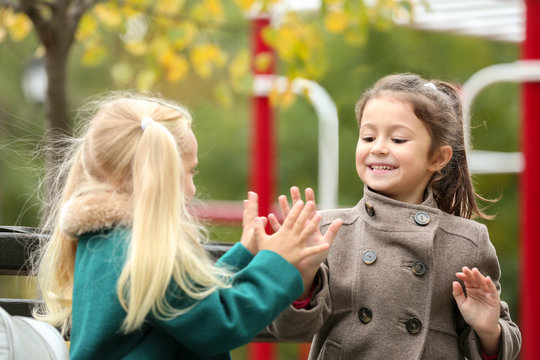 Cute little girls in outwear sitting and playing on bench outdoors