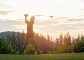 Fototapeta na wymiar Asian woman golf player doing golf swing tee off on the green sunset evening time, she presumably does exercise. Healthy and Lifestyle Concept.