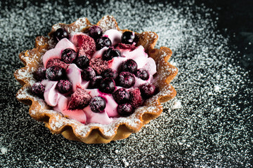 Fresh fruit and berry tart dessert with toss sugar on wooden background. Delicious sweet cake with raspberries, figs, strawberries, cherry, and cream.