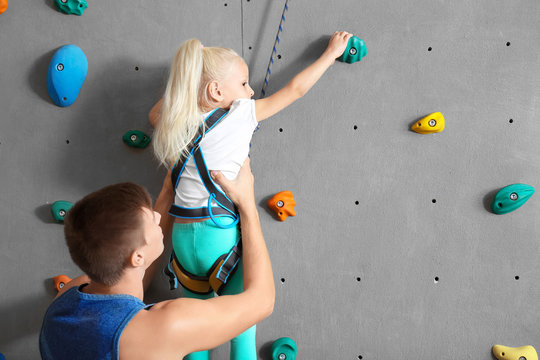 Instructor helping little girl climb wall in gym