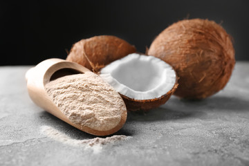 Wooden scoop with coconut flour and fresh nuts on table