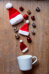 Obraz na płótnie Canvas White cup on lying on side with Santa Claus hat and baubles