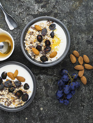 Breakfast from healthy seasonal ingredients: granola, flakes, honey, dark grapes, almonds in a serving gray pial on a gray grunge background. Top view. Vegetarian Organic Food Concept.