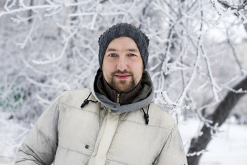 Fototapeta na wymiar Young man in a white down jacket on the background of snowy forest