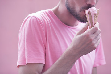 Pink obsession concept. Outdoor closeup fashion portrait of young hipster guy eating melting ice...