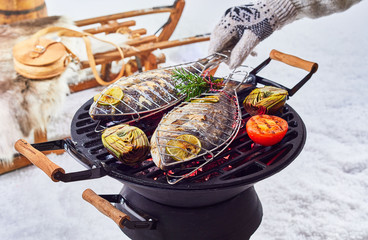 Two whole fish grilling over a winter barbecue