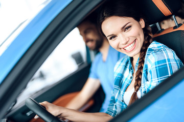 A woman is sitting at the wheel of a new car.