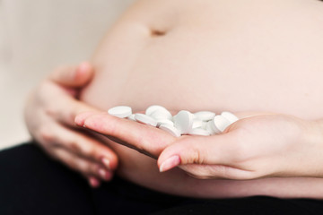 pregnant woman holding white pills or vitamins in hand