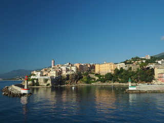 Fototapeta na wymiar Corsica Bastia port view from sea on harbour with red and green lighthous church and old town blue sky background