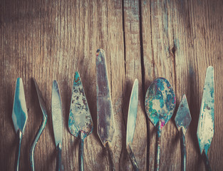 Row of artist palette knifes on old wooden rustic backdrop, retro styled.