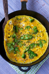 Omelette with broccoli and herbs, toasted with sesame seeds on frying pan. View from above, top, vertical