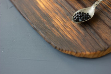 Fresh black caviar in a metal spoon on wooden board.