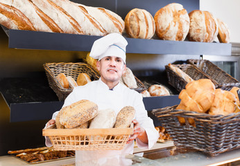 Male employee offering fresh baguettes and buns in bakery
