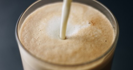 Mixing coffee, hot chocolate and steamed milk into a large glass to make a hot drink on light gray background