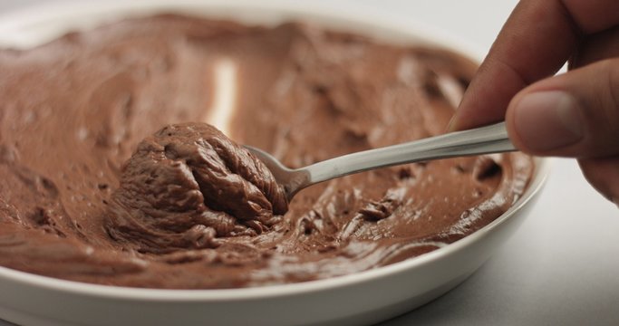 Soft spongy chocolate mousse taken out of a stainless steel pan with a teaspoon isolated on white