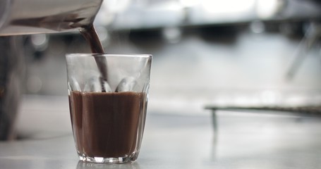 Close up of a barista in an industrial looking cafe making hot cocoa drinks in glass tumblers
