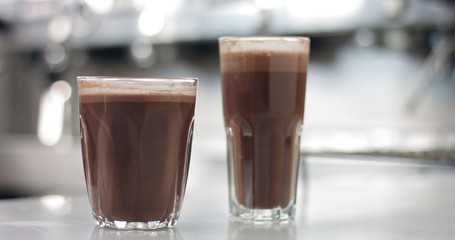 Close up of a barista in an industrial looking cafe making hot cocoa drinks in glass tumblers