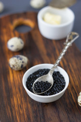 Metal spoon with fresh black caviar over the wooden board.