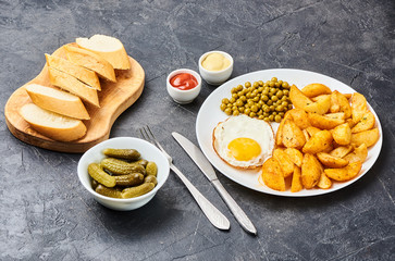 Fried potatoes with fried eggs, green peas on concrete gray background