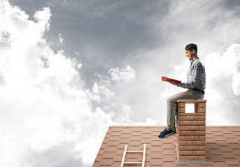 Handsome man on brick roof against cloud scape reading book