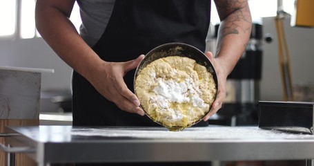 Dark skinned male chef in a black apron works with bread dough in an industrial looking kitchen