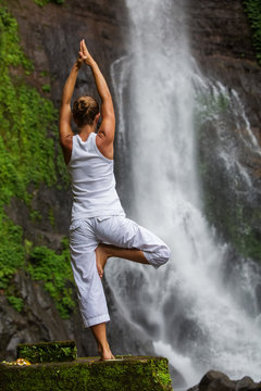 Woman practices yoga at Gitgit waterfall on Bali in indonesia