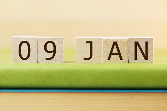 Wooden cube shape calendar for JAN 9 on green book, table. 