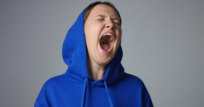 Young woman in large unlabeled bright blue hoodie screams and acts scared and angry showing stress