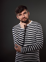 Bearded happy emotional man thininking about with fun grimacing face on grey background. Closeup portrait