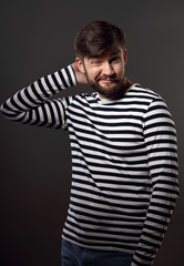 Obraz premium Bearded happy emotional man thininking and scratching the head with fun grimacing face on grey background. Closeup portrait