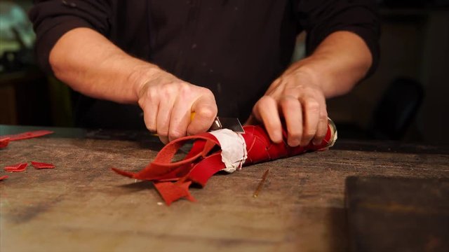 Professional works on a table with a knife on a new accessory. He cuts excess piece of leather off the accessory.