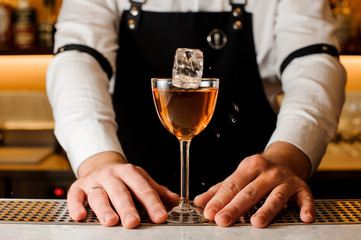 Barmans hands holding a glass with alcoholic drink and ice cube